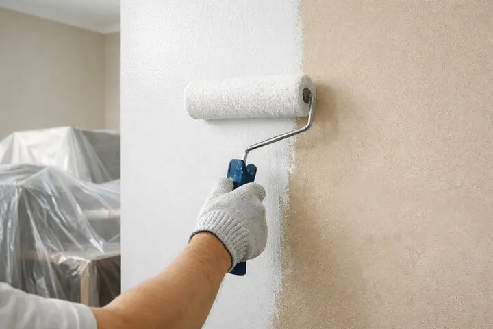 Interior wall being painted with a roller, showing how often should you repaint the interior of your home based on wall condition and wear