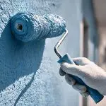 Painter applying exterior paint with roller illustrating factors that affect the timeline of an exterior painting project