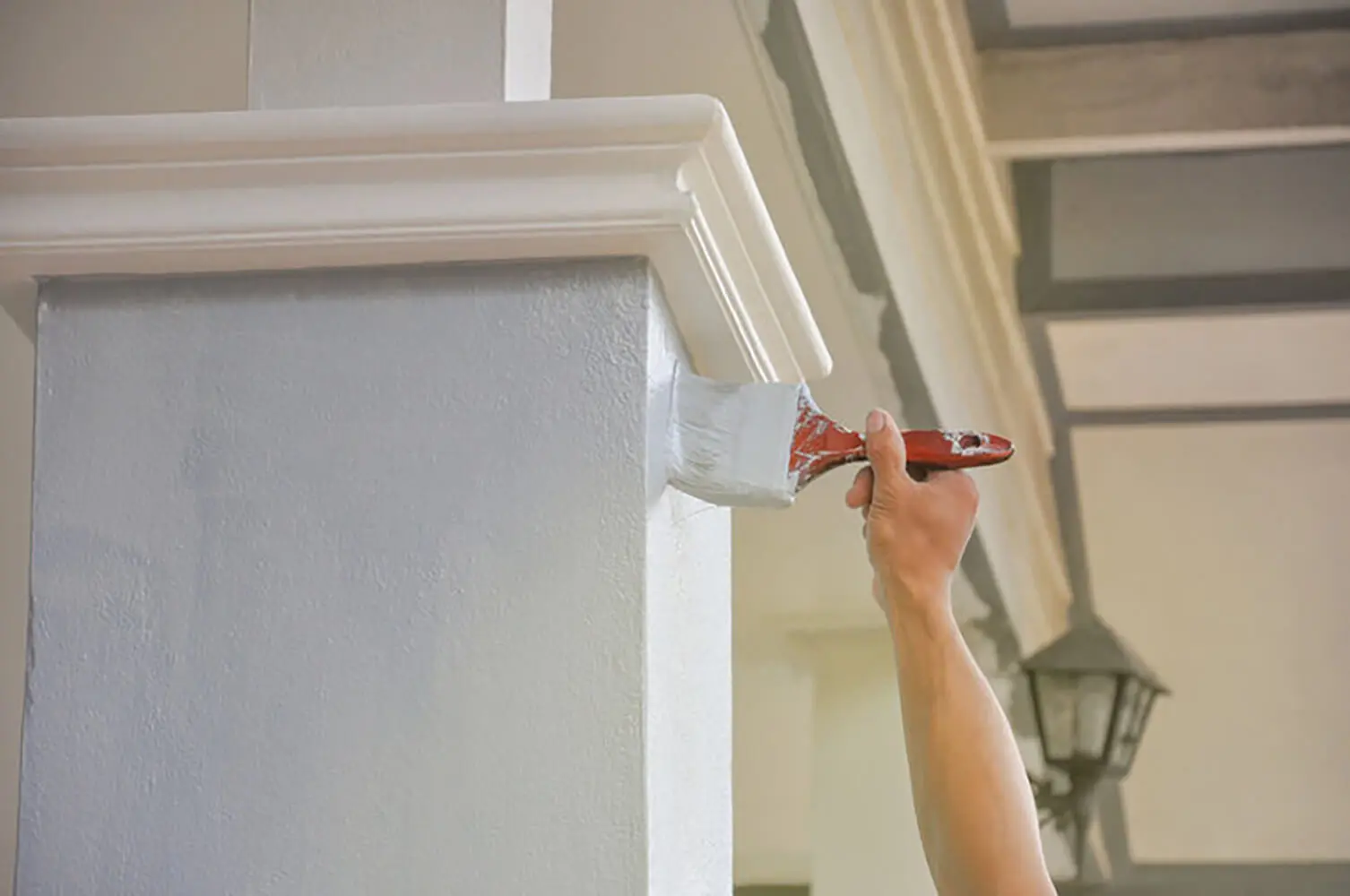 Painter applying white paint to exterior trim, showing how exterior painting quotes are calculated based on surface area and detail work