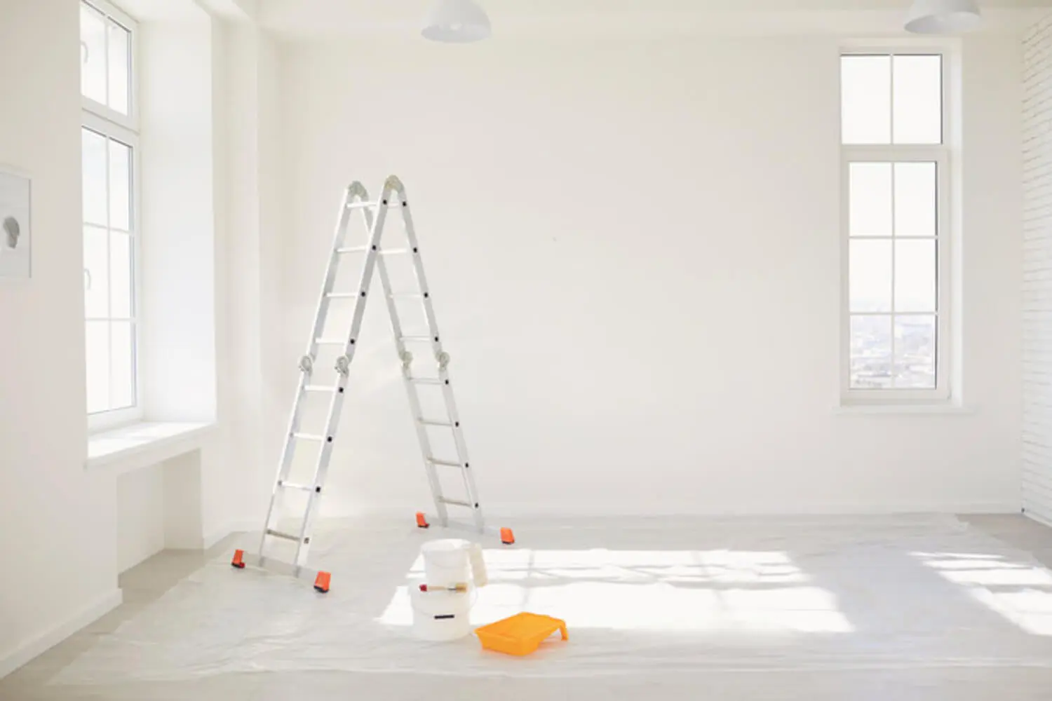 Bright, sunlit room prepped for interior painting with a ladder and supplies near large windows.