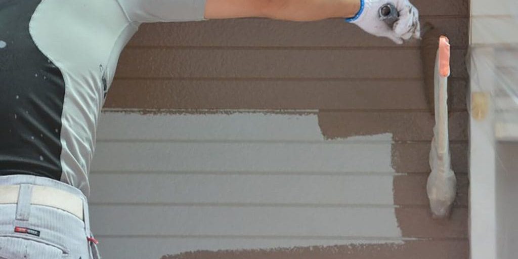 Painter applying extreme paint colors in Oklahoma weather to exterior siding, demonstrating coverage and durability during a professional exterior paint job