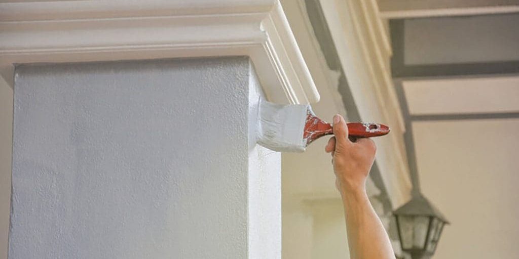 Painter applying white paint to exterior trim, showing how exterior painting quotes are calculated based on surface area and detail work