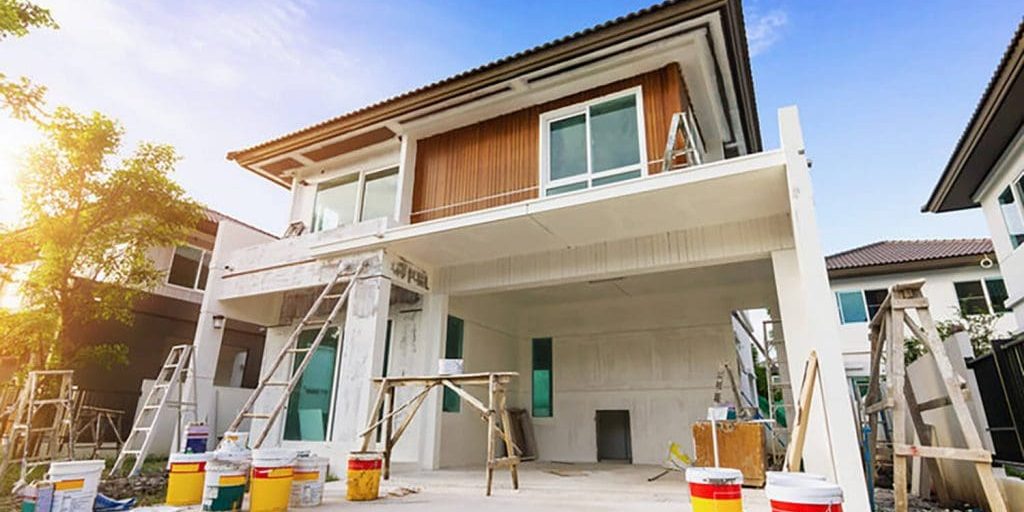 Exterior house during painting preparation with ladders, scaffolding, and paint buckets set up around the home